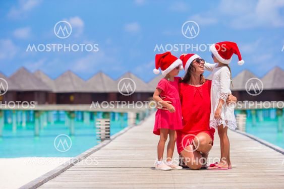 Happy mother and little girls in Santa hat near water villa on summer vacation