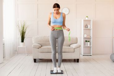 Shocked Girl Measuring Waist With Tape Standing On...