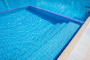 Bright blue swimming pool reflecting sunlight,...