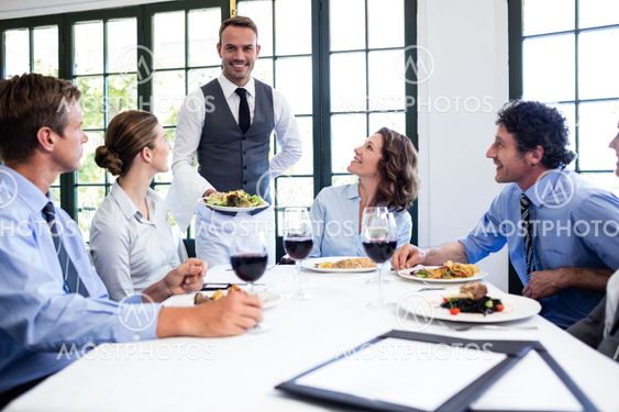 Waiter serving salad to business people