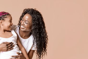 Happy woman cuddling her little daughter and looking...