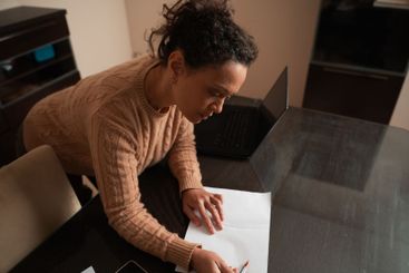Woman concentrating on writing at desk with open laptop...