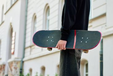 Skateboarder holding worn skateboard walks at street