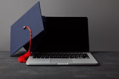 Laptop with blank screen and academic cap with red tassel...
