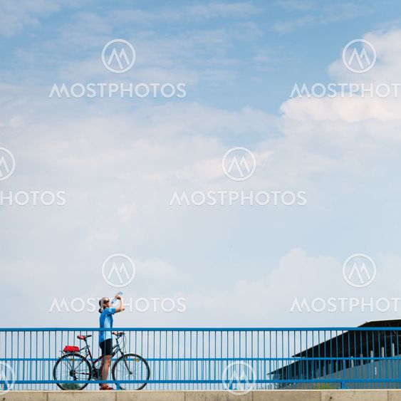 Background for poster or advertisment pertaining to cycling/sport/outdoor activities - female cyclist during a halt on a bridge against blue sky (color toned image)