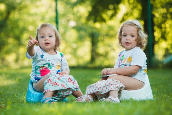 The two little baby girls sitting on pottys against green...