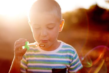 Bubbles, face and boy in field with fun, sunset...
