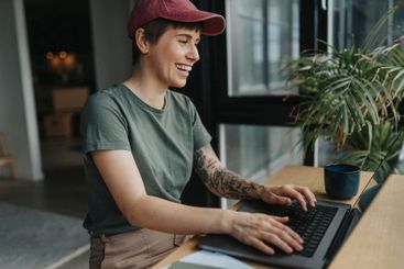Happy businesswoman with tattooed arm working on laptop...
