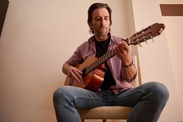 Man playing acoustic guitar indoors wearing casual...
