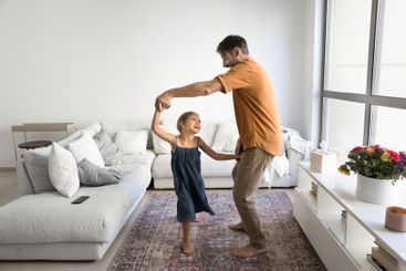 Father and little daughter holding hands, dancing at home