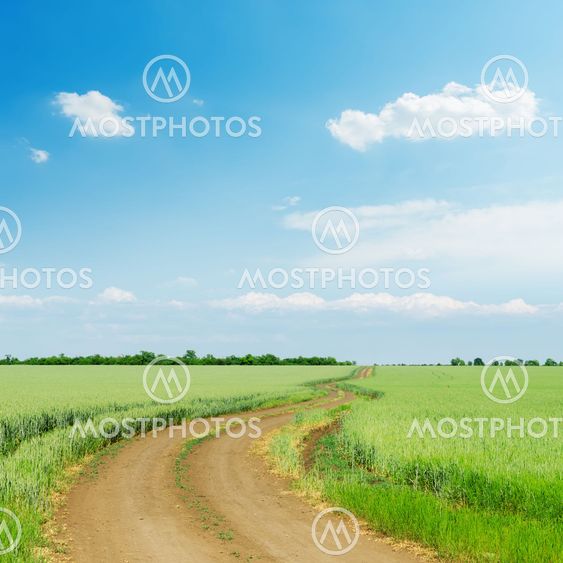 dirty road in green agriculture field and blue sky with...