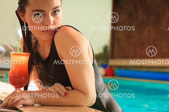 Girl with cocktail drink at swimming pool edge.