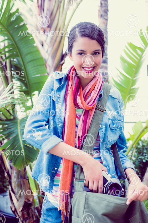 Young happy woman taking camera out from her bag outside