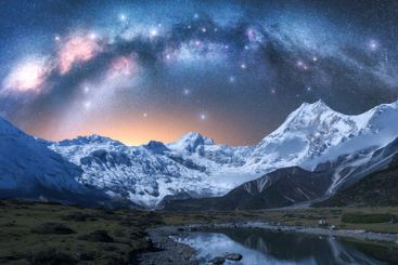 Milky Way arch over snowy mountains and lake at night in...