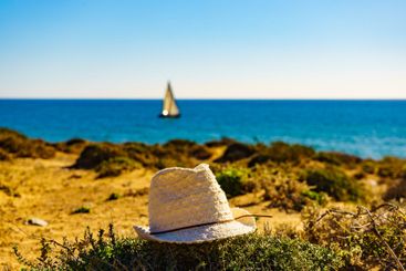Coast view with summer hat and yacht sailing on sea