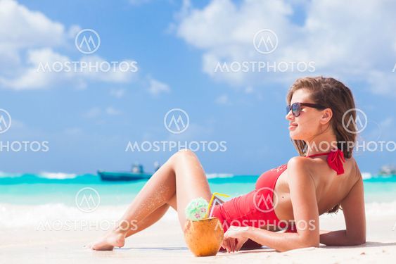 young woman in swimsuit and straw hat in sunglasses with coconut on beach