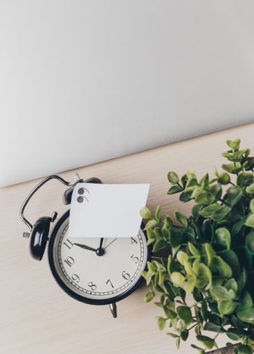 Clock and plant on wooden table with note in home office...