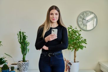 Confident young woman with smartphone in home interior