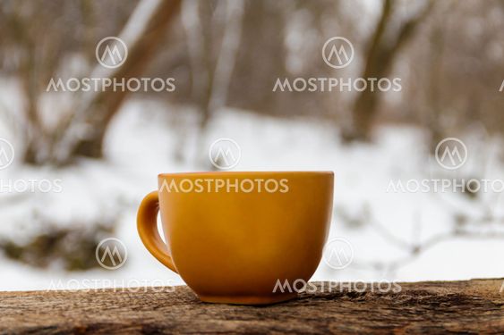 Orange cup of coffee on the background of the winter forest