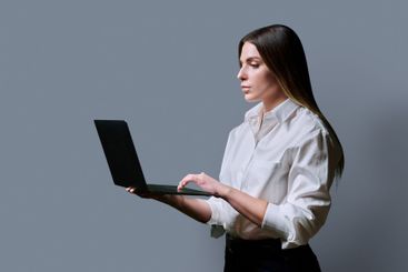 Profile view, young woman using laptop on grey studio...
