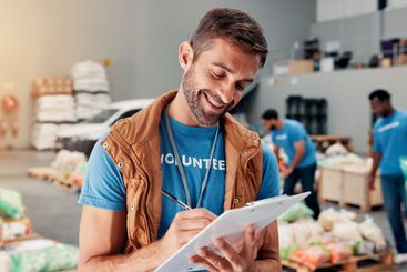 Volunteer, writing and clipboard with man in warehouse...