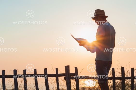 Young hipster man exploring map over the sunset at seaside