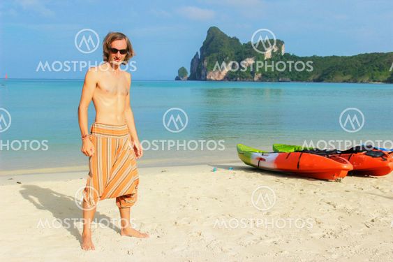 young topless man standing in front of a row Kayaks canoes boats on the PhiPhi Don beach in Thailand