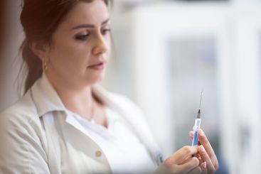A focused nurse in a white lab coat carefully prepares a...