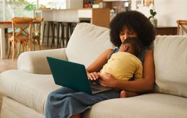 Mother Working on Laptop While Holding Baby in Cozy...