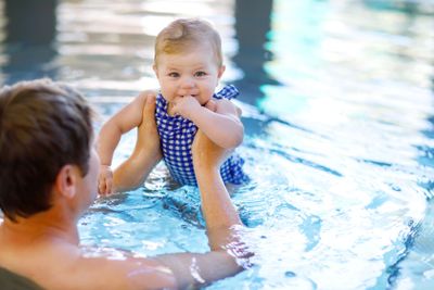 Happy middle-aged father swimming with cute adorable baby...