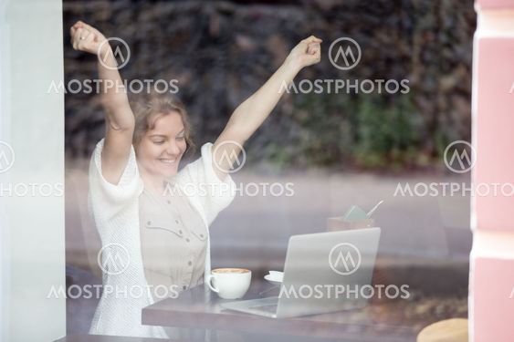Portrait of happy woman in coffee shop celebrating success with her hands up