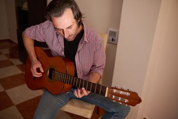 Man playing an acoustic guitar while seated in an indoor...