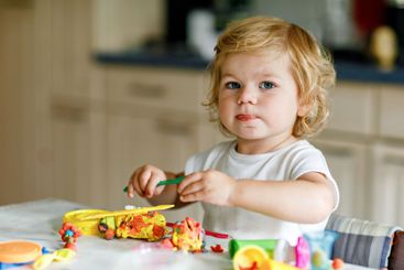 Adorable cute little toddler girl with colorful clay at...