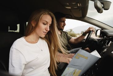 Young loving couple on a road trip using map inside a car