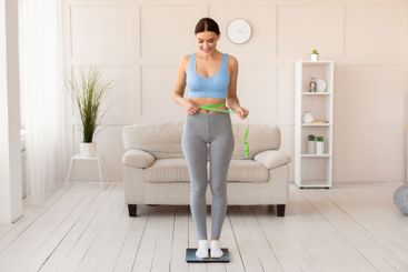 Woman Measuring Waist Standing On Scales Slimming At...