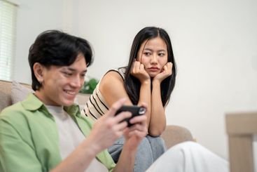 A moody Asian girl sits in the living room, feeling...