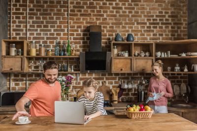 Cute little girl using laptop with parents in kitchen