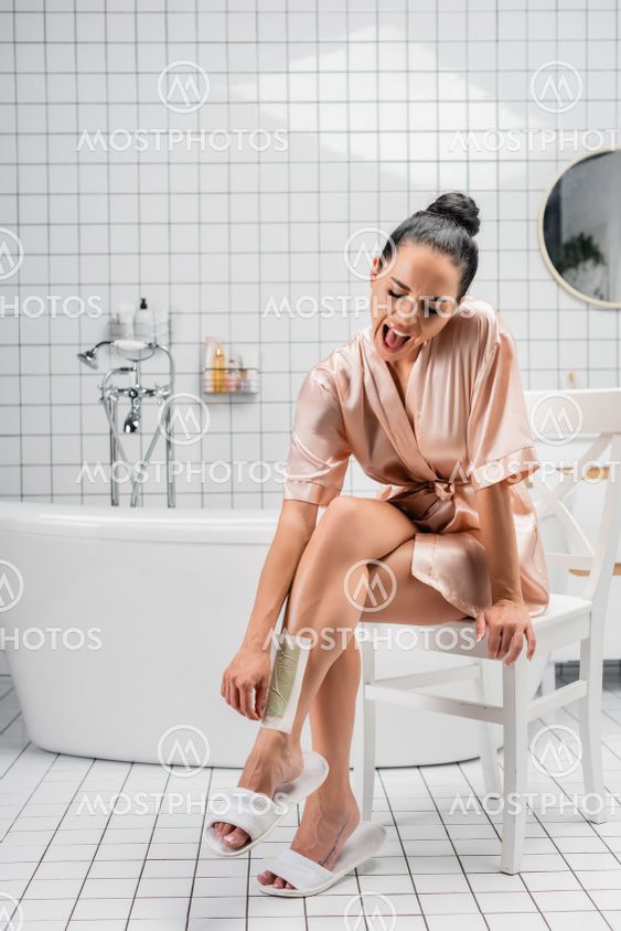 Screaming woman in silk bathrobe taking off depilation...