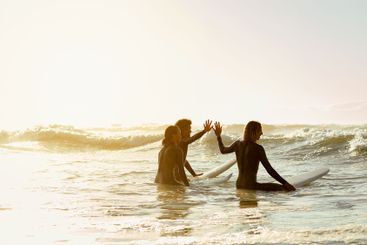 High five, surfer group and friends in sea ready for...