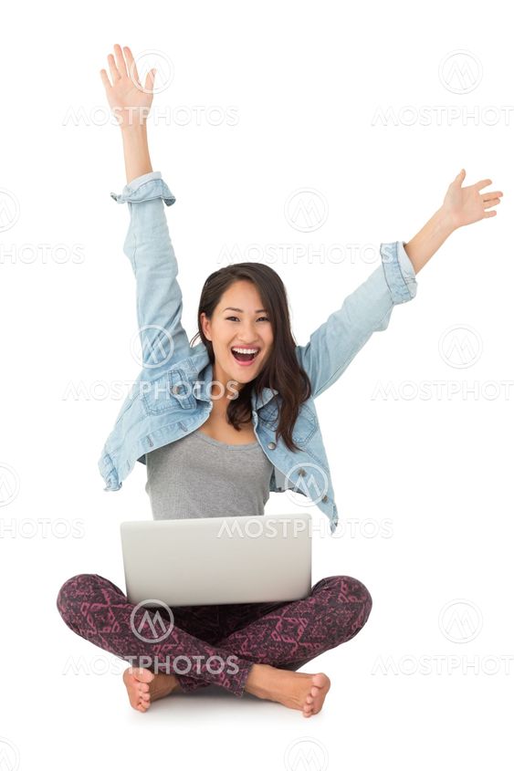 Asian woman cheering at camera with laptop sitting on floor