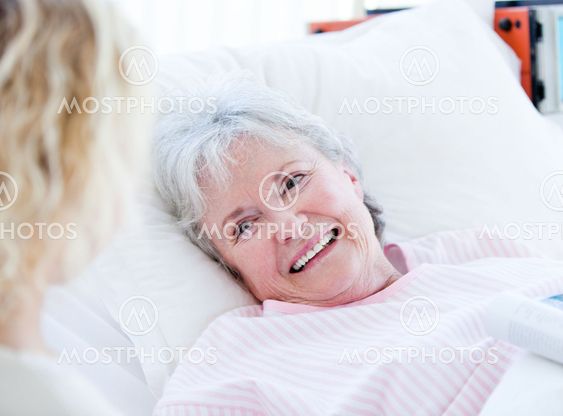 Smiling senior woman lying on a hospital bed talking with her granddaughter