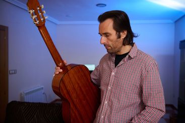 Man holding a classical guitar in a warmly lit indoor...