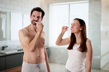 Smiling couple brushing teeth in bathroom together