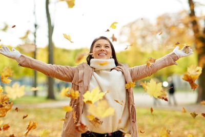 happy woman having fun with leaves in autumn park