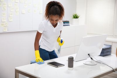 Female Janitor Cleaning Desk In Office