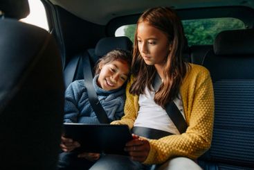 Sisters sharing tablet PC while sitting in car during...