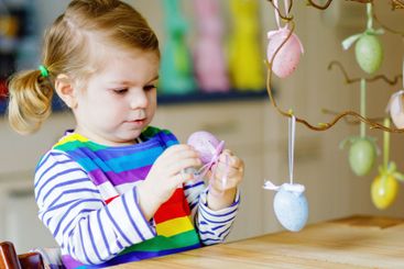 Cute little toddler girl decorating tree bough with...