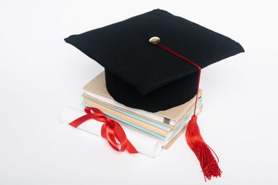 Black graduation cap with red tassel on top of books and...