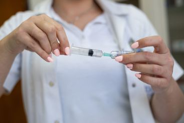 A focused nurse in a white lab coat carefully prepares a...