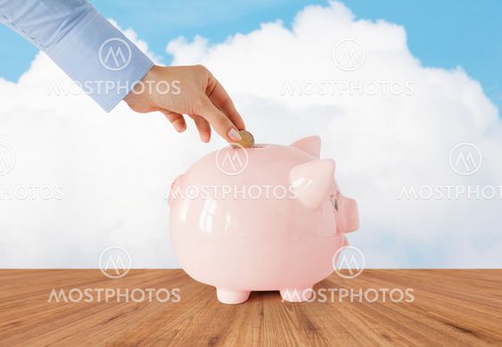 close up of hand putting coin into piggy bank